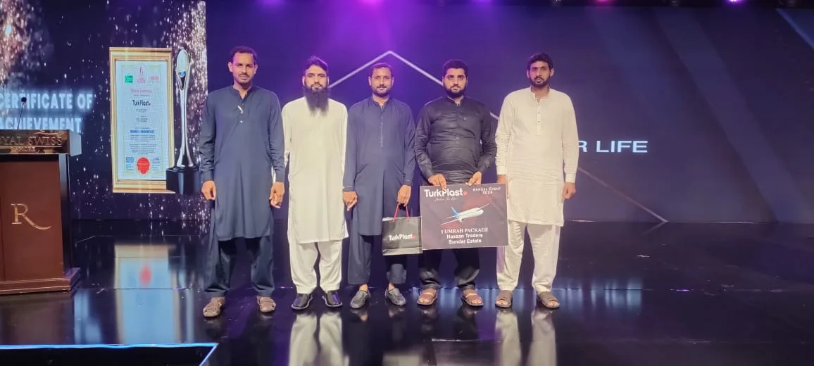 The Hassan Traders team on stage at the TurkPlast annual event 2024, holding the Umrah package award, with a certificate of achievement on the screen behind them