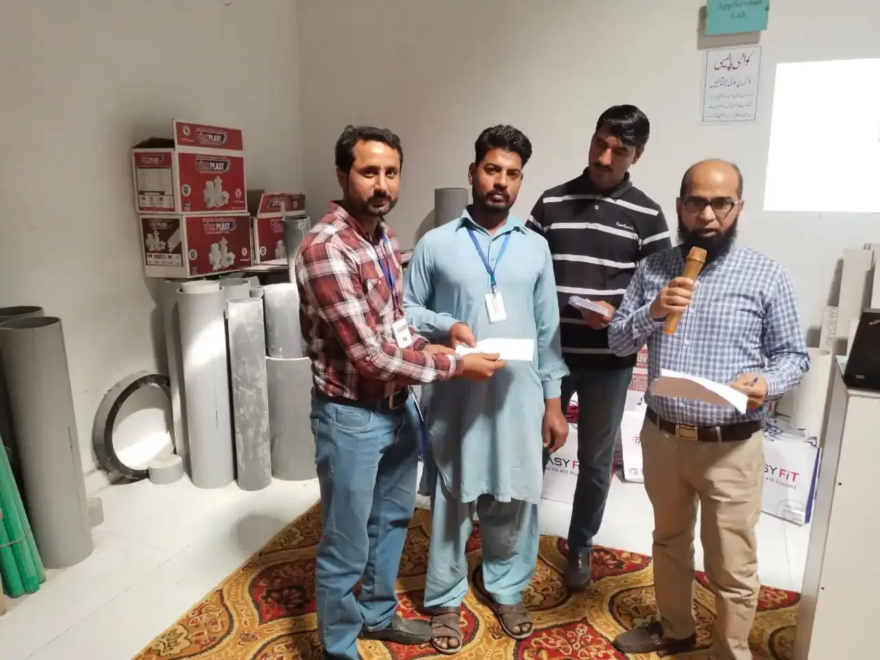 Men with lanyards receive envelopes at a TurkPlast and Easyfit event, TurkPlast boxes and Easyfit bags around the room